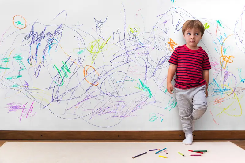 boy standing infront of a wall with colorful scribbling