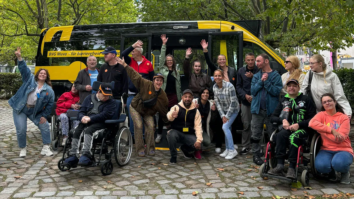 Gruppenfoto beim Inklusions-Event mit Menschen im und am BVG Muva. Ein gelber Shuttlebus bildet den Rahmen, im Vordergrund Rollstühle und Teilnehmende – sichtbares Zeichen für barrierefreie Mobilität in Berlin und unsere Event-Organisation.